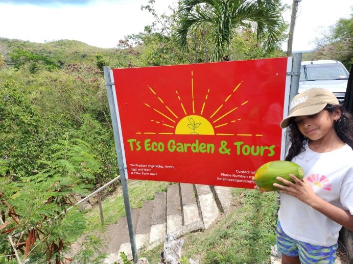A guest holding a coconut beside the T’s EcoGarden farm sign